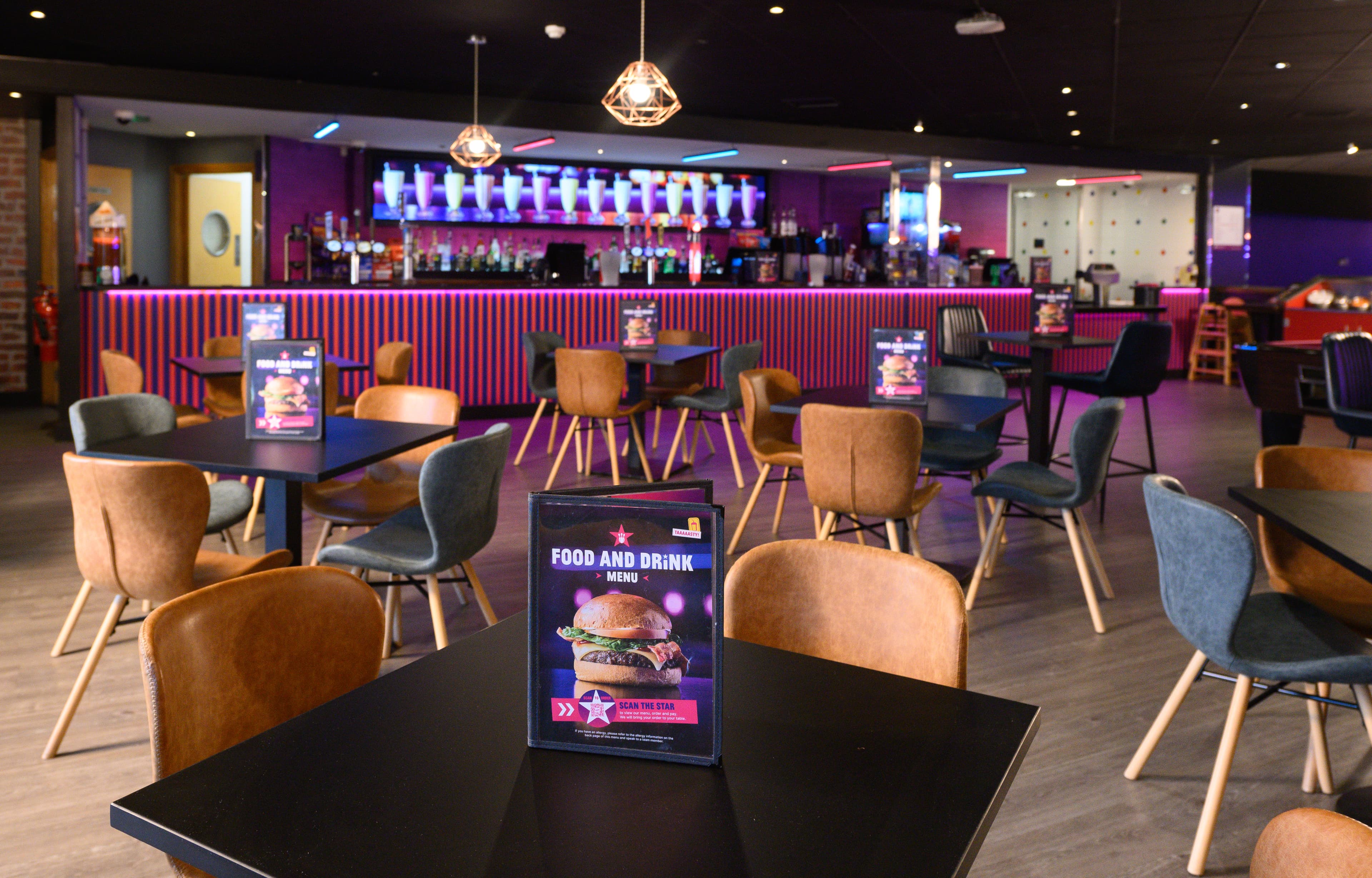 The bar area. Lots of tables and chairs. There is a menu on each table. Behind it is the bar area.